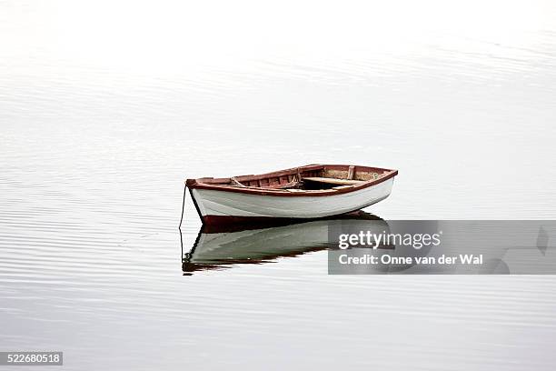a small white dinghy rests at anchor in quiet water. - kleines wasserfahrzeug stock-fotos und bilder