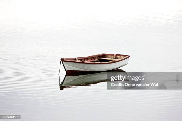 a small white dinghy rests at anchor in quiet water. - rowboat bildbanksfoton och bilder