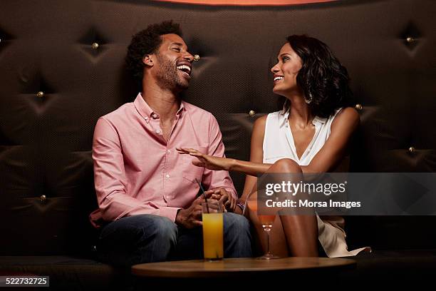 cheerful couple conversing on sofa at nightclub - flirten stockfoto's en -beelden