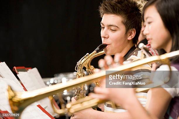 teenage boy playing saxophone in high-school band - high performance stockfoto's en -beelden