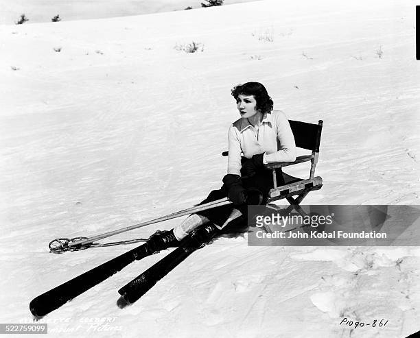 Portrait of actress Claudette Colbert resting in a chair on a snow slope, whilst wearing skis, for Paramount Pictures, 1932.