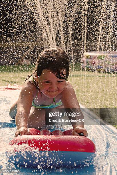 girl playing on a slip and slide in the back garden - backyard water slide stock pictures, royalty-free photos & images