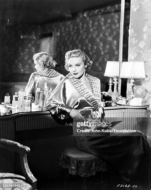 Portrait of actress Madeleine Carroll sitting at a dressing table and wearing a silk robe, with Paramount Pictures, 1936.