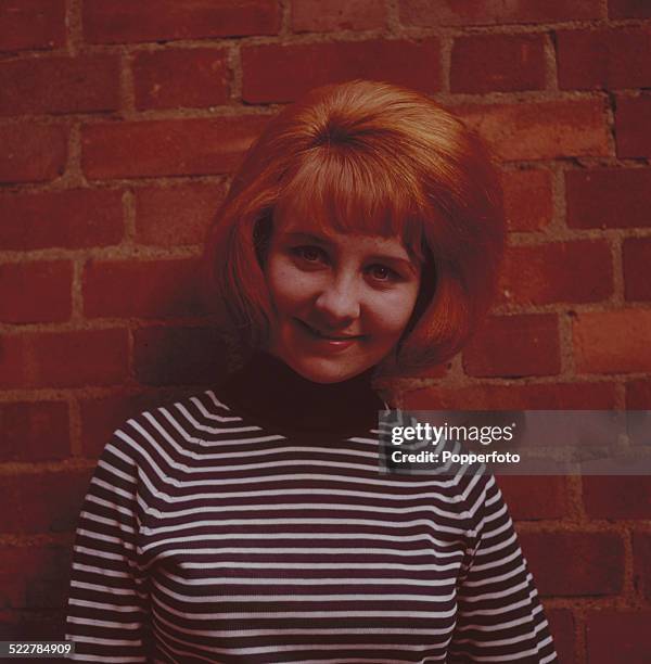 Scottish singer Lulu posed wearing a striped top whilst standing in front of a brick wall in 1964.