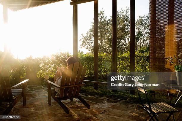 woman relaxing with coffee and a book on veranda. - mirador fotografías e imágenes de stock