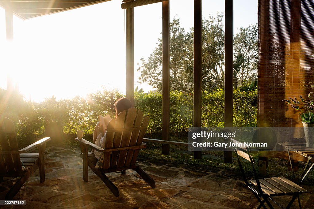 Woman relaxing with coffee and a book on veranda.