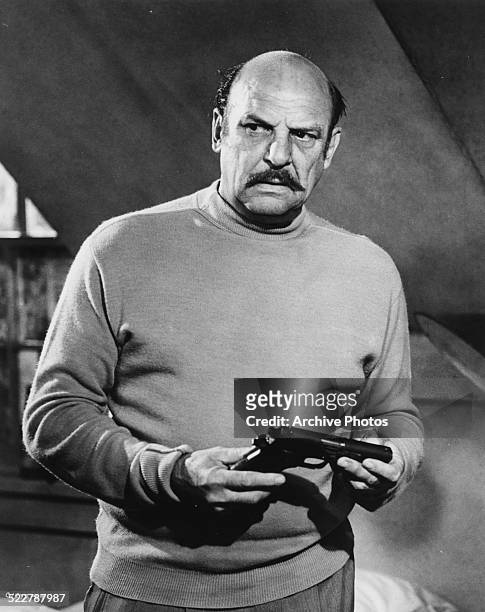 Portrait of actor Jackie Coogan holding a gun, in a scene from the movie 'Marlowe', 1969.