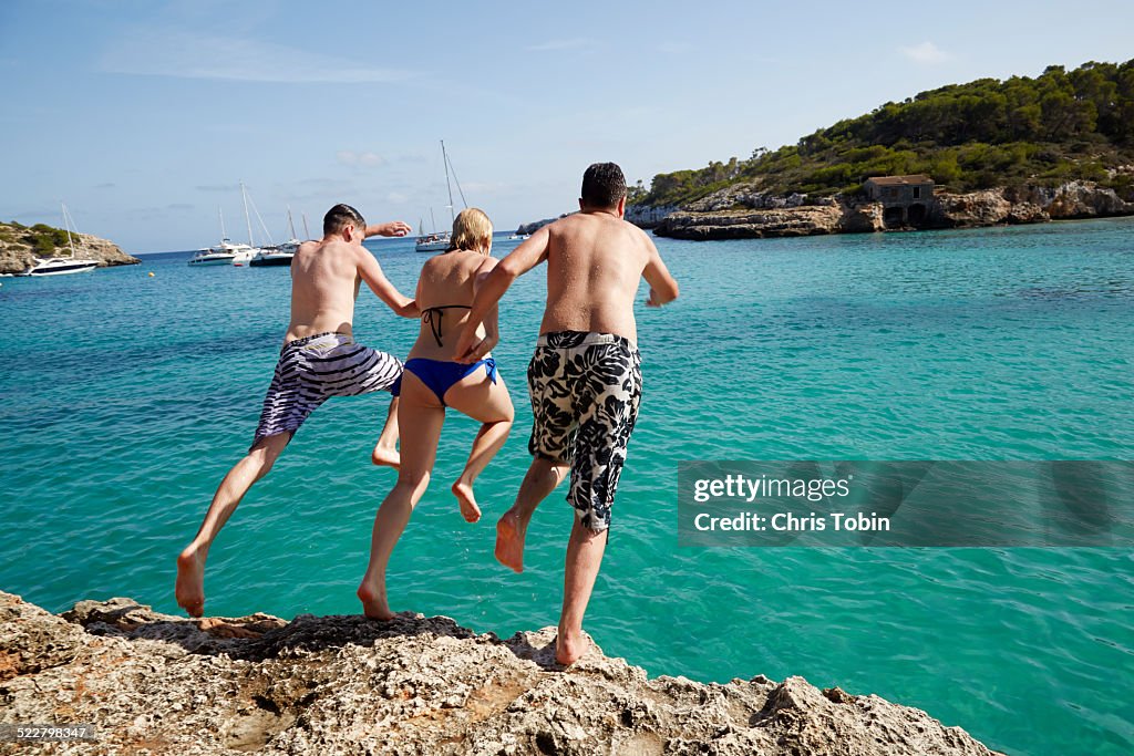 Group of friends jumping off rock into sea