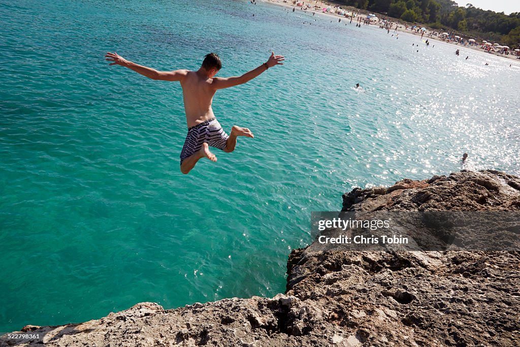 Young man jumping off rock at beach