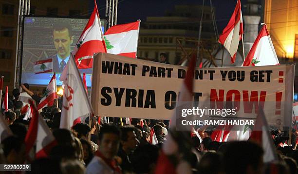 Lebanese opposition protesters wave their national flags and banners calling for the Syrian withdrawal from Lebanon as they watch live on a giant...