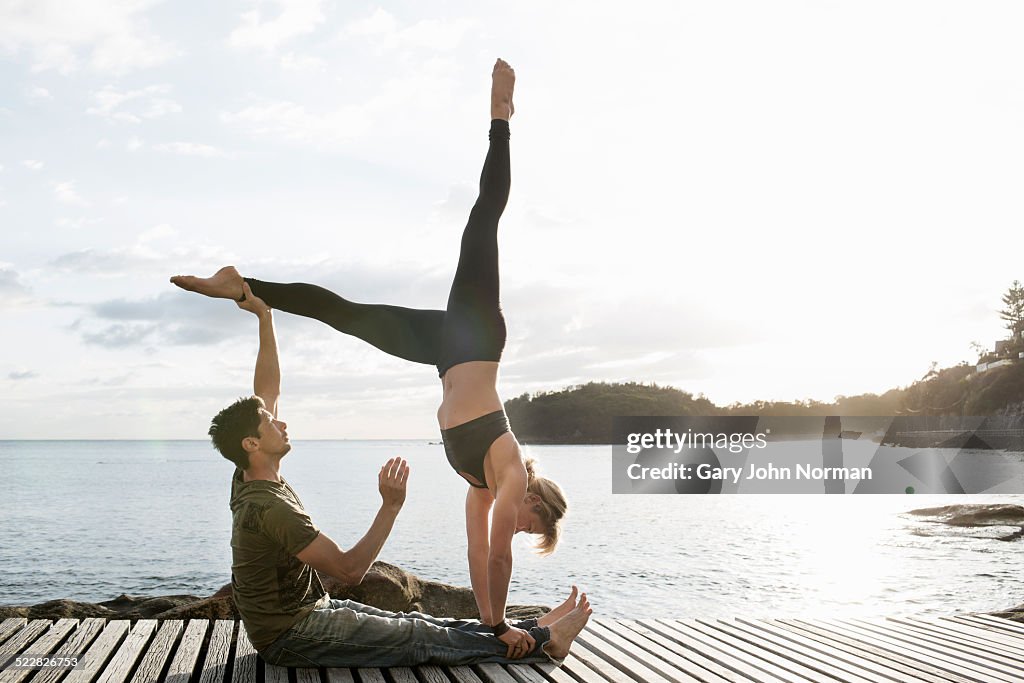 Couple practicing yoga on wooden deck.