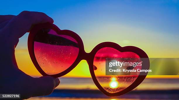 beautiful sunset through heart-shaped sunglasses on beach - flamingo heart stock pictures, royalty-free photos & images