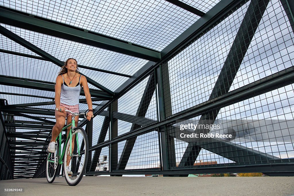 A young, happy adult woman riding her bicycle on an urban bridge