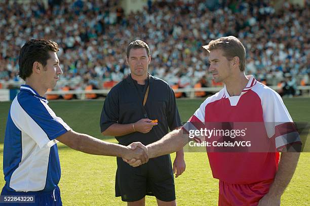 two soccer players shake hands in front of referee at start of soccer match - game 27 23 stock pictures, royalty-free photos & images