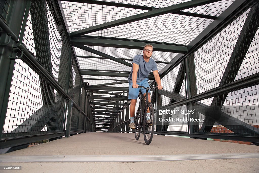 A young, happy adult man riding his bicycle on an urban bridge