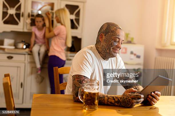 lächelnd tätowiert mann mit touchpad in der küche. - tablet alcohol stock-fotos und bilder
