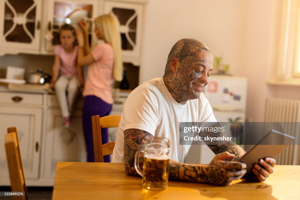 Smiling tattooed man using touchpad in the kitchen.