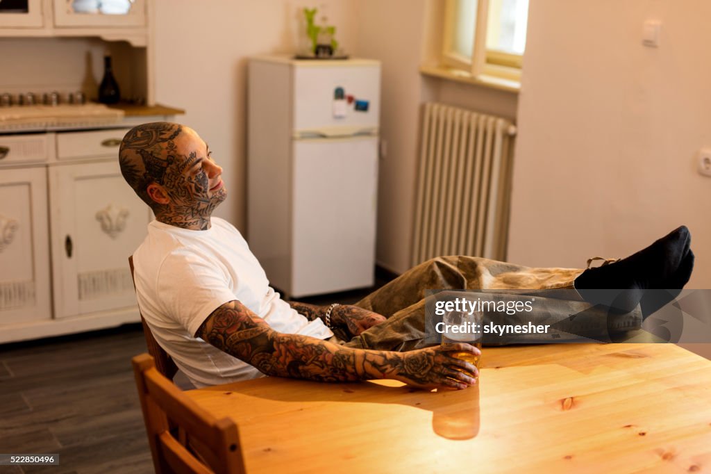 Tattooed man relaxing in the kitchen with feet up.