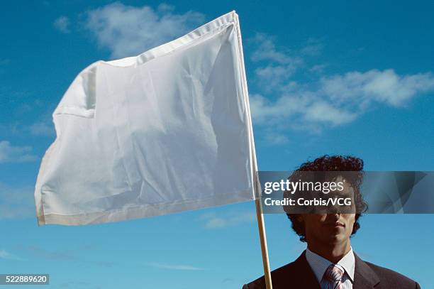 portrait of a businessman holding a white flag against blue sky - white flag stockfoto's en -beelden