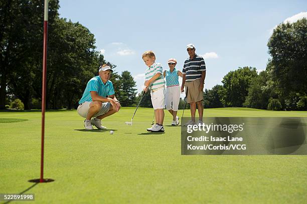 boy (6 years) playing golf with family observing him - putting clothes son stock pictures, royalty-free photos & images