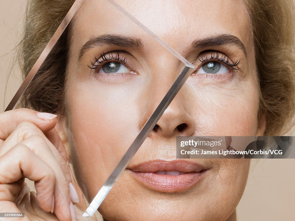 Studio shot of smiling middle-aged woman with younger skin viewed through glass