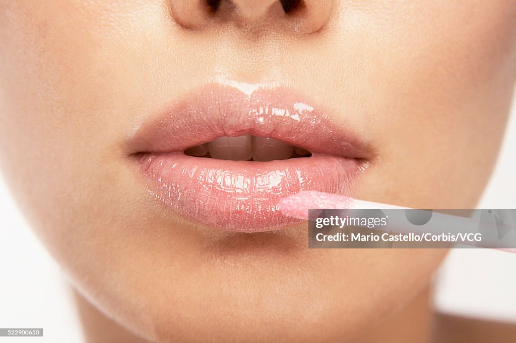 Young woman applying pink lipgloss