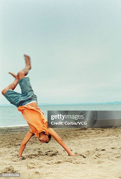 boy doing a cartwheel on the beach against blue sky - boy handstand stock pictures, royalty-free photos & images