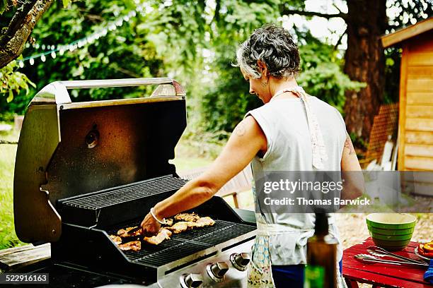 smiling woman grilling chicken on barbecue - grilled stock pictures, royalty-free photos & images