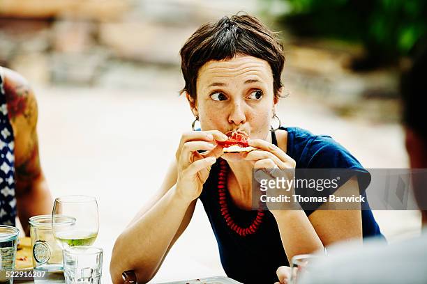 woman taking bite of pizza during backyard dinner - indulgence stockfoto's en -beelden