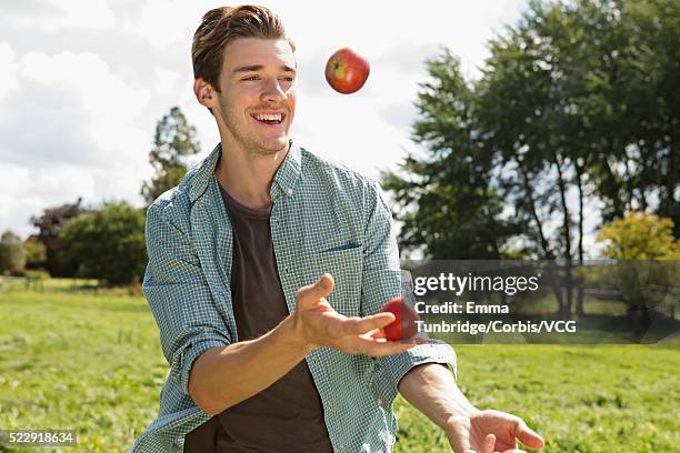 young man juggling apples in park, uk - corbis historical stock-fotos und bilder