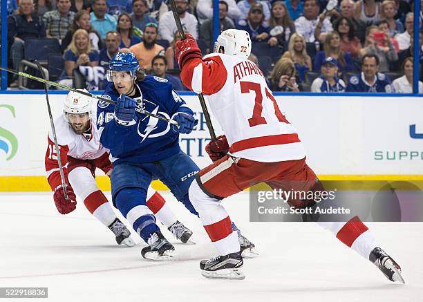 Michael Blunden of the Tampa Bay Lightning skates against Riley Sheahan and Andreas Athanasiou of the Detroit Red Wings during the third period of...