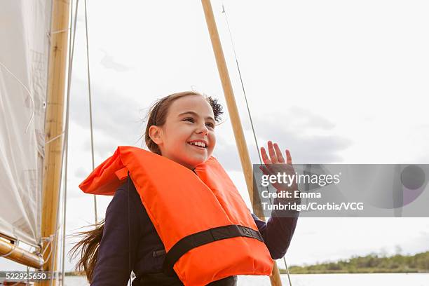 girl (6-7) in life jacket on sailboat waving - waving stock-fotos und bilder