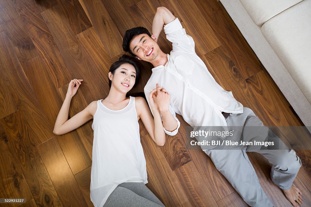 Young couple holding hands lying on wooden floor