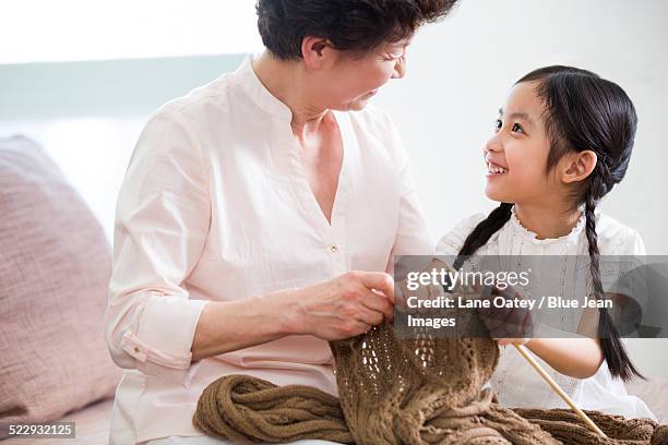 happy grandmother and granddaughter knitting in living room - old granny knitting stock-fotos und bilder