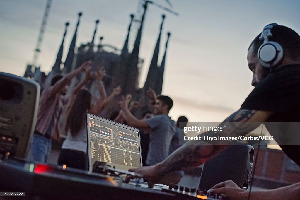Disc jockey playing on roof terrace with group of people dancing in background