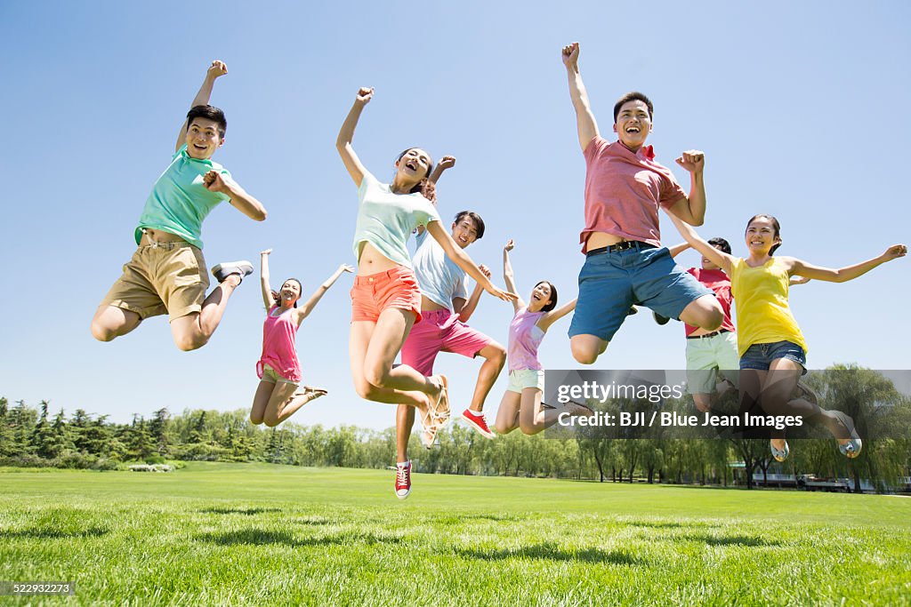 Cheerful young adults jumping on grass