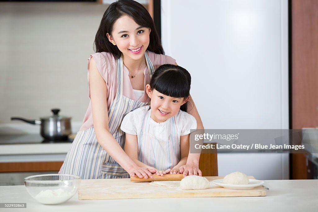 Happy mother and daughter rolling out dough