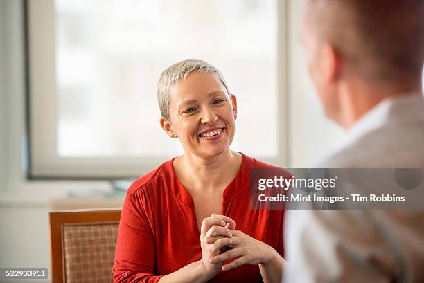 a woman with her hands clasped smiling at a man. - red dress shirt stock pictures, royalty-free photos & images