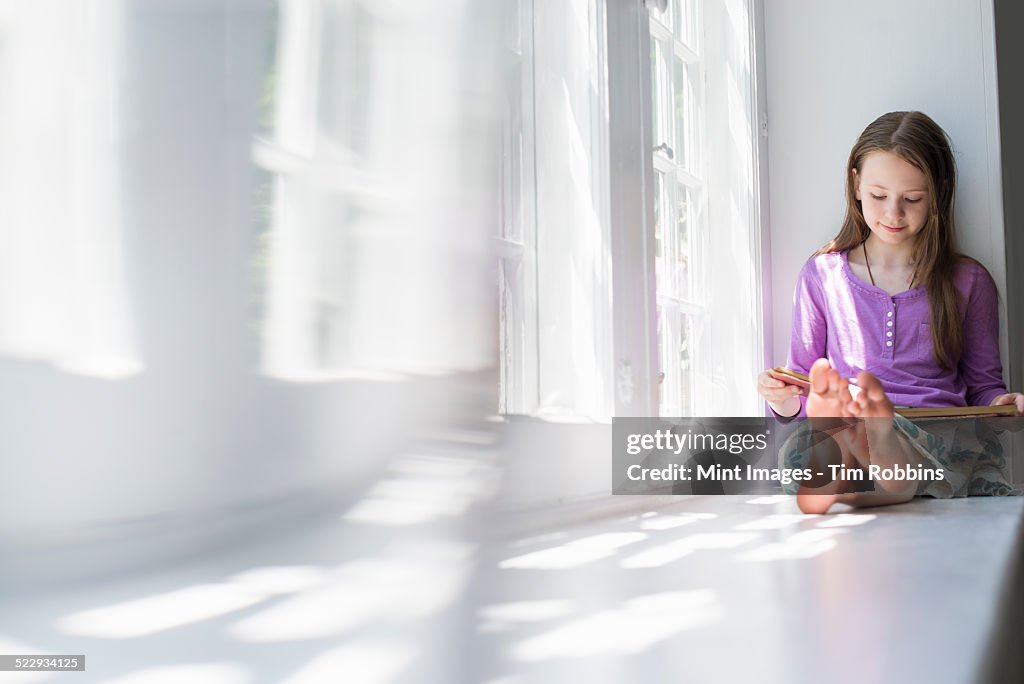 Girl sitting by a window, reading a book.