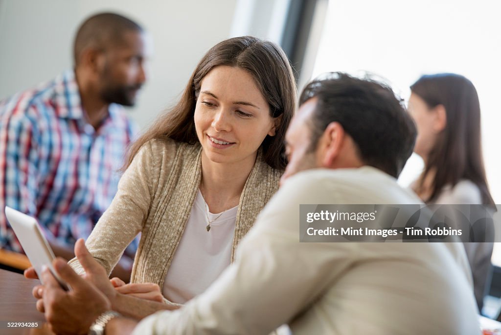 Four people in an office, two men and two women, a couple looking at the screen of a digital tablet.