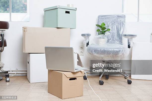 stack of cardboard boxes, wrapped swivel chair and a notebook in an office - behelfsmäßig stock-fotos und bilder