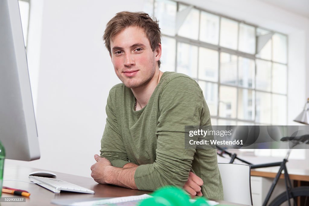 Portrait of smiling young man sitting at his desk in the office