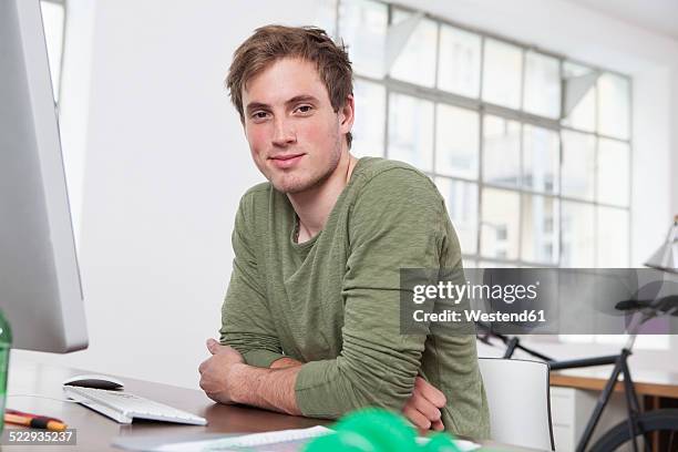 portrait of smiling young man sitting at his desk in the office - 18 19 anos - fotografias e filmes do acervo