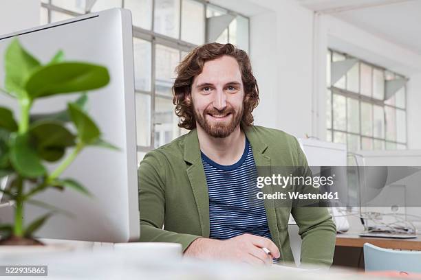 portrait of young man sitting at his desk in a creative office - münchen immobilie büro stock-fotos und bilder