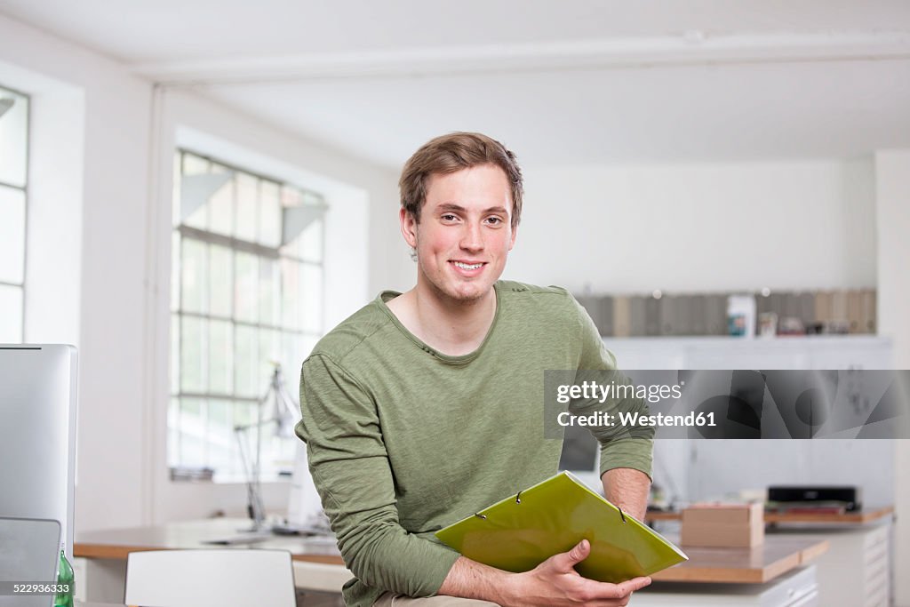 Portrait of smiling young man sitting on his desk in the office