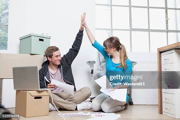 two colleagues sitting on ground between cardboard boxes in an office giving high five - makeshift office stock pictures, royalty-free photos & images