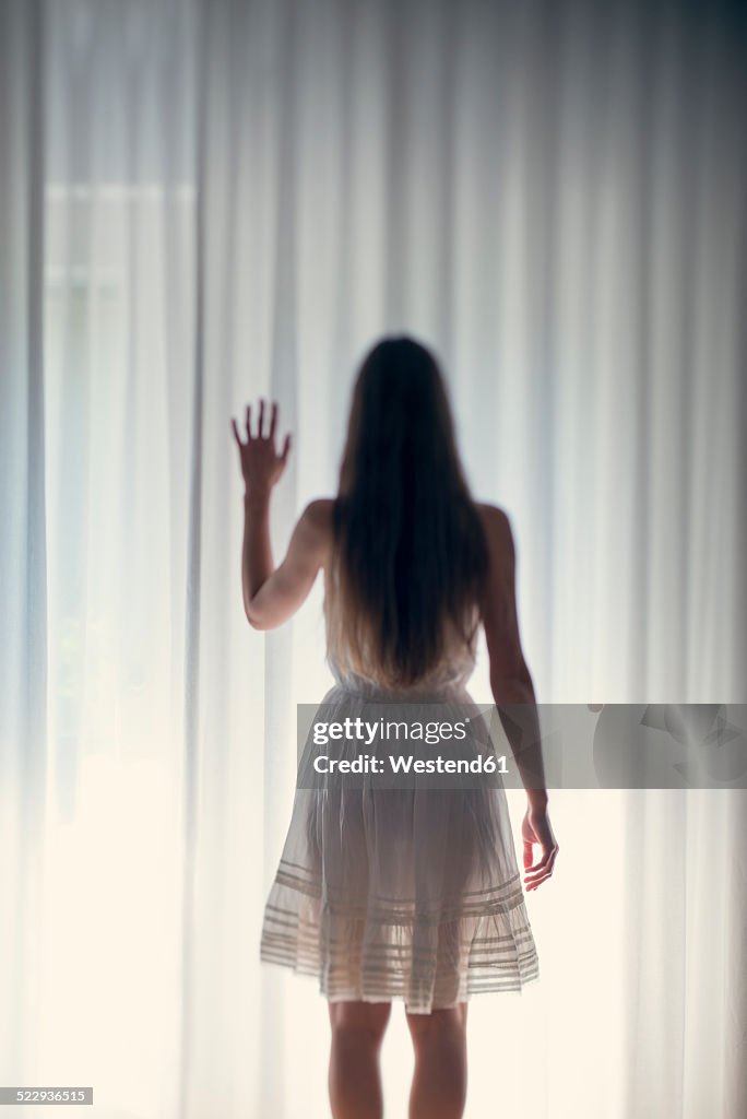 Mystical young woman standing in front of a white curtain, back view