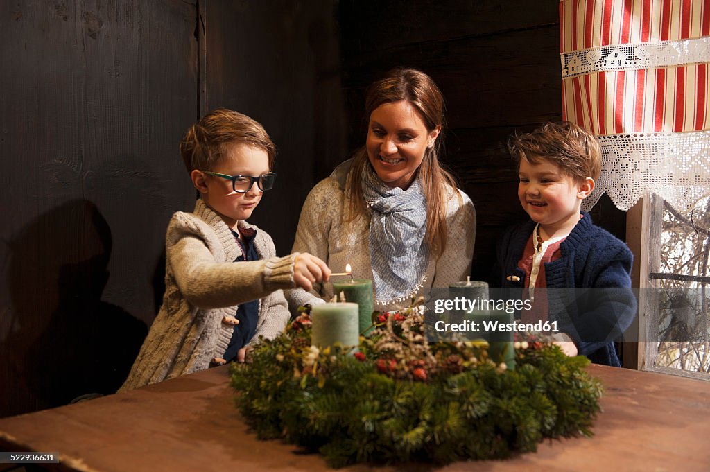 Mother with her two little sons lightning candles on a Advent wreath