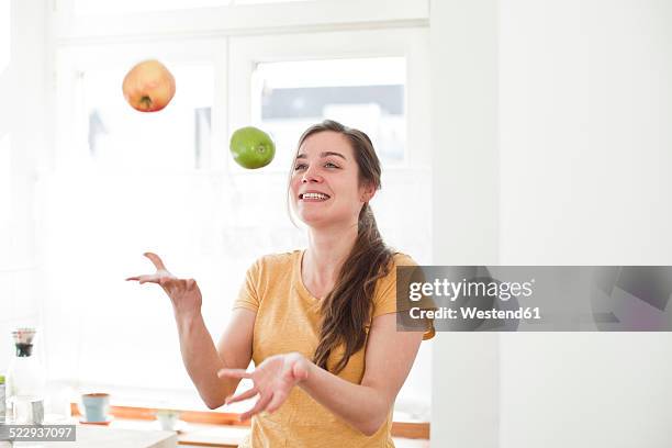 smiling young woman juggling with two apples in her kitchen - juggling stock pictures, royalty-free photos & images