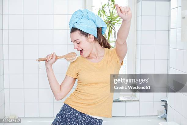 portrait of young woman singing in the bathroom using massage brush as microphone - bad body language stockfoto's en -beelden